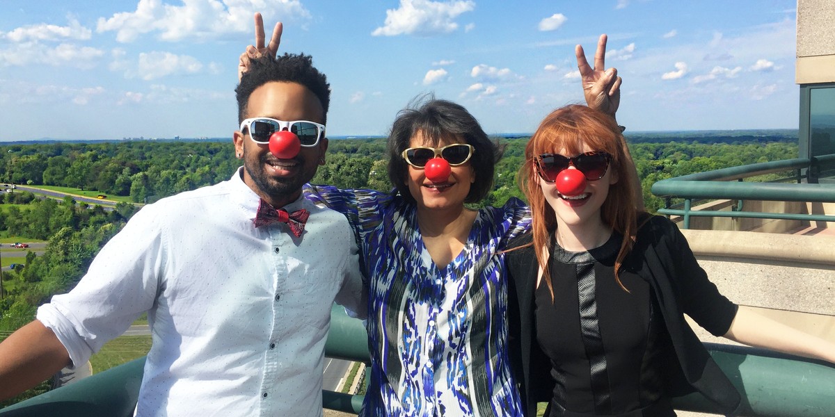 Group of three people standing on a balcony with clown noses.