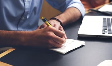 Businessman writing a note on paper in front of a laptop.