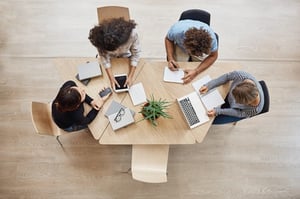 Open office space with people working around a table with laptops.