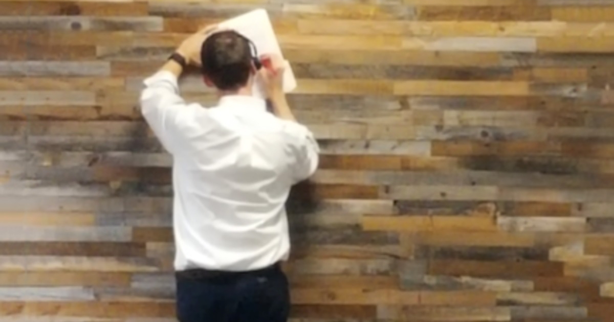 Man in a white business shirt writing on a document leaning against a wall.