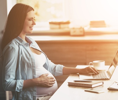 Pregnant woman typing on a laptop.